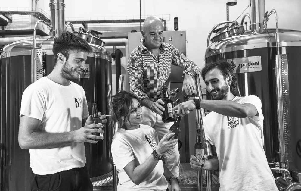 Il team del birrificio posa sorridente con le proprie birre davanti agli impianti.