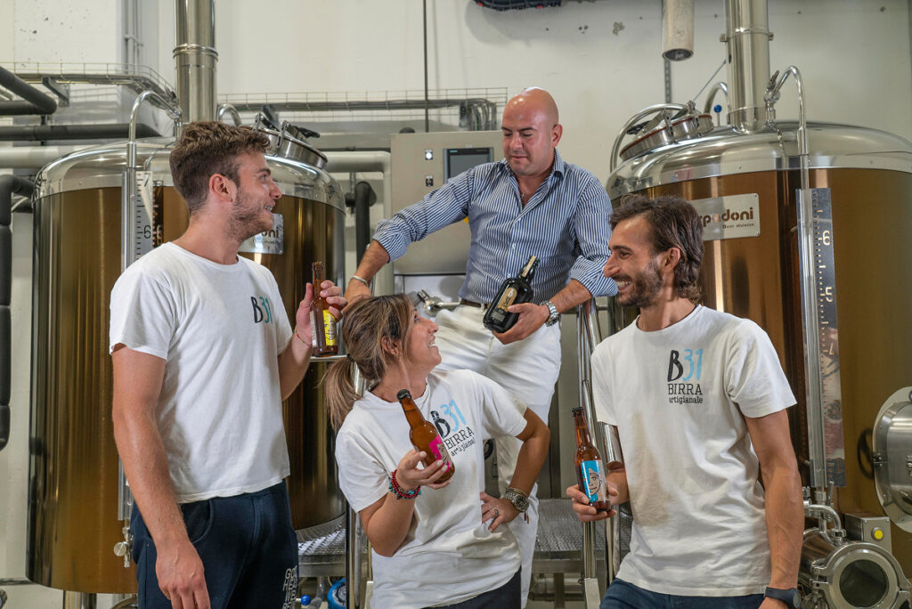 Il team del birrificio posa sorridente con le proprie birre davanti agli impianti.